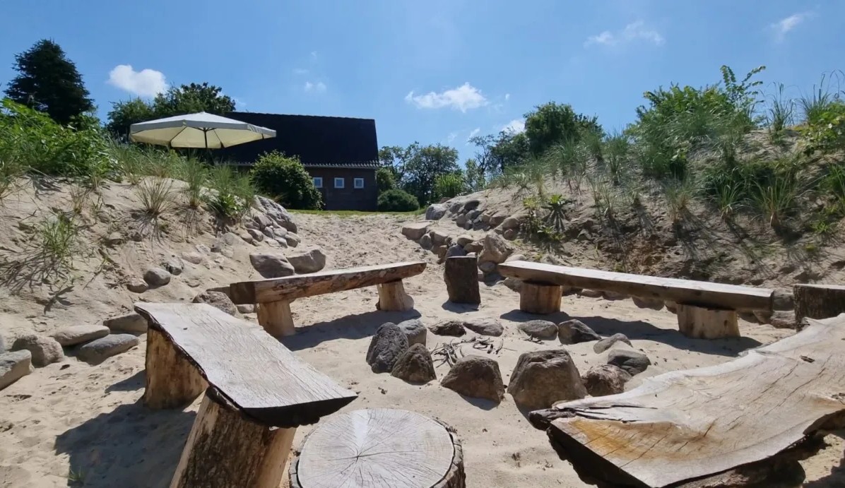Feuerstelle mit Holzbänken in der Düne, das Haus im Hintergrund
