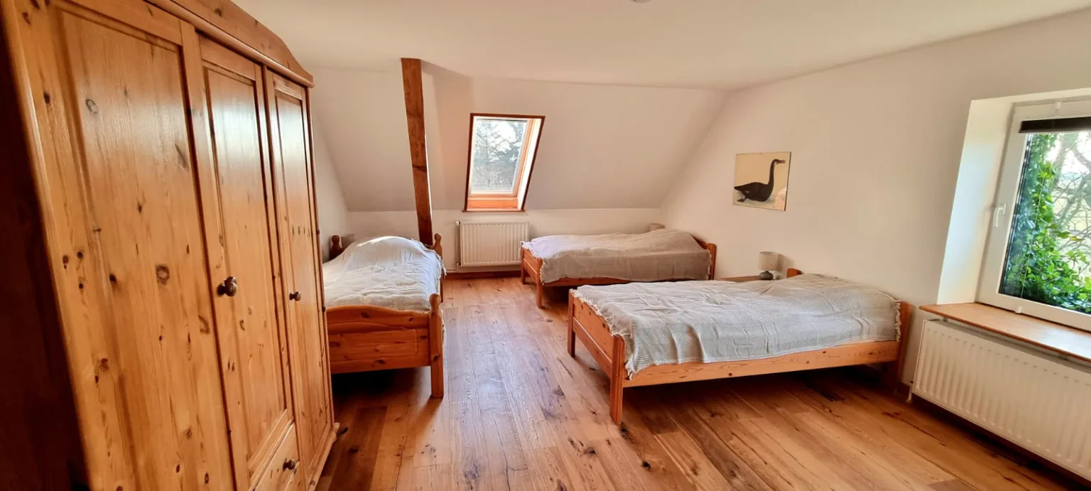 Helles Mehrbettzimmer mit Holzboden unter dem Dach