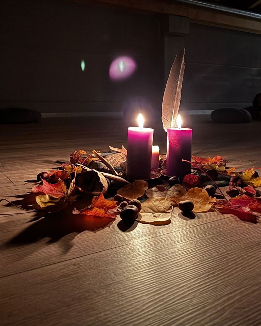 Brennende Kerzen, eine Feder und Herbstlaub auf dem Boden
